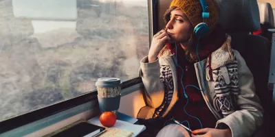 Een vrouw gekleed in winterkleding met print kijkt uit een raam van de trein terwijl ze een koptelefoon draagt